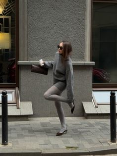 Woman in a gray sweater and tights posing on a city street