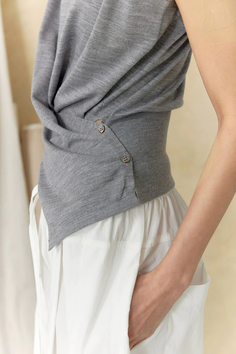 Person in a gray sleeveless top and white pants with hand in pocket