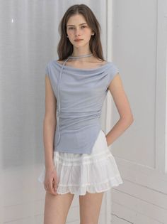 Woman with long hair wearing a light blue top and white mini skirt indoors