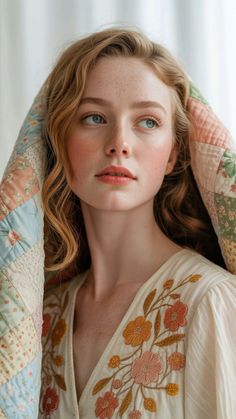 Woman with red hair and freckles wearing an embroidered dress, holding a quilted blanket