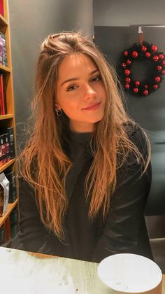Woman with long hair and a turtleneck in an indoor setting with a Christmas wreath