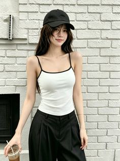 Woman in a white camisole and black cap standing against a brick wall