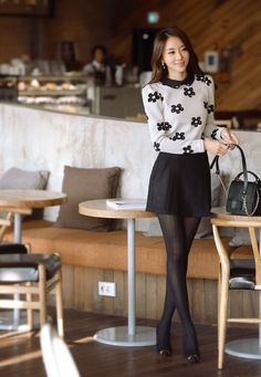 Woman in a floral sweater and black skirt standing in a cafe