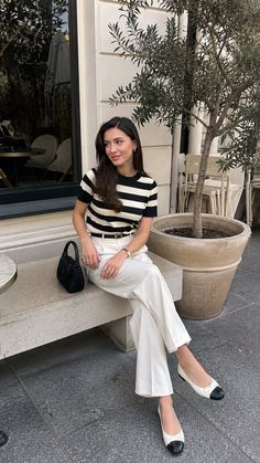 Woman in a striped shirt and white pants sitting outdoors
