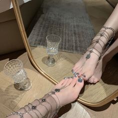 Feet adorned with silver chain anklets and glitter nail polish reflected in a mirror