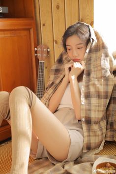 Woman in a plaid shirt and shorts sitting indoors with a ukulele