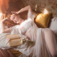 Woman with red hair in sheer lingerie lying on a bed with a book and flowers