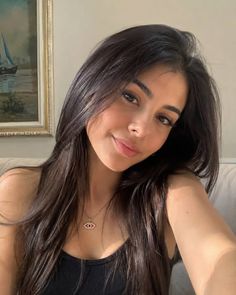 Woman with long dark hair wearing a black top and necklace indoors