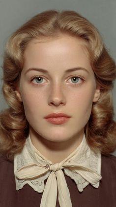Woman with blonde hair and blue eyes wearing a brown top with a lace collar