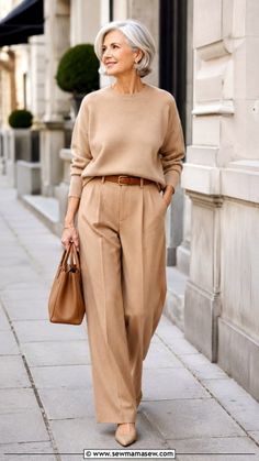 Woman with short gray hair in a tan sweater and wide leg pants walking outdoors