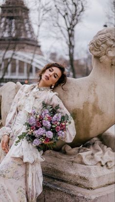Woman in a floral dress holding a bouquet, leaning on a statue with the Eiffel Tower in the background