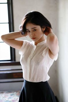 Woman in a white shirt and black skirt with hands behind her head