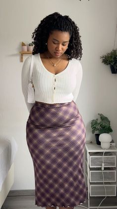 Woman with curly hair wearing a white cardigan and plaid skirt indoors