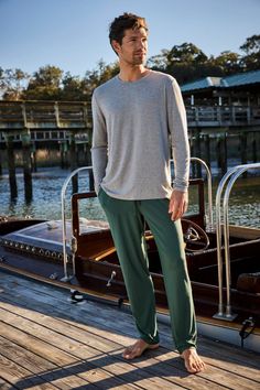 Man in a gray long sleeve shirt and green pants standing barefoot on a wooden dock