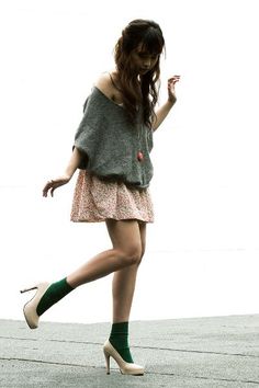 Woman in a floral skirt, green socks, and high heels against a white background