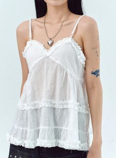 Woman in a white ruffled top with a heart locket and visible tattoos