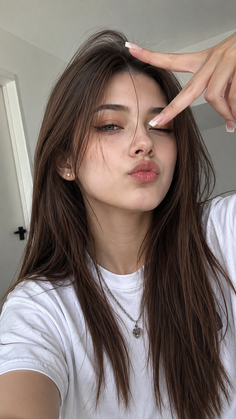 Young woman with long brown hair making a kissy face and pointing at her eye