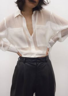 Woman in a sheer white shirt and black pants with hands on hips