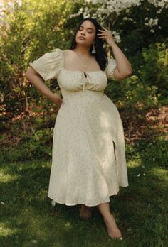 Woman in a floral dress standing barefoot on green grass outdoors