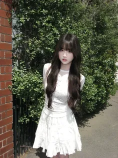 Woman with long dark hair in a white dress standing outdoors