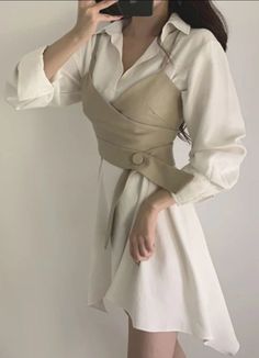 Woman in a white shirt dress with a beige corset top, holding a phone