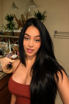 Woman with long black hair wearing a red top indoors