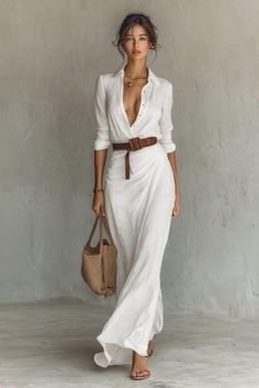 Woman in a white dress with a deep V-neck and a brown belt holding a straw bag