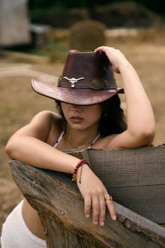Woman in a cowboy hat and white bikini top leaning on a wooden fence