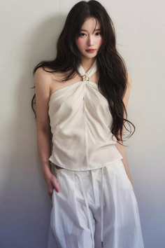Woman with long black hair wearing a white halter top and white pants indoors