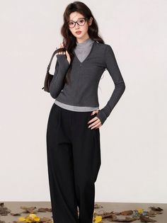 Woman in a gray top and black wide-leg pants with a handbag and glasses