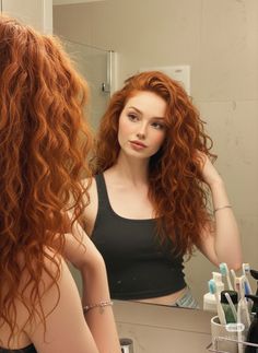 Woman with long curly red hair looking at her reflection in a mirror