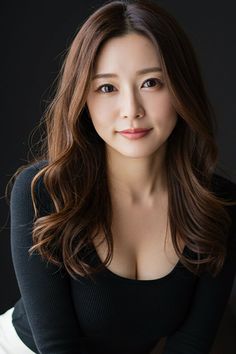 Woman with long brown hair wearing a black top with visible cleavage