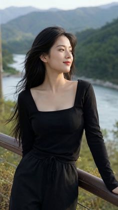 Woman with long black hair in a black top looking out over a river and mountains