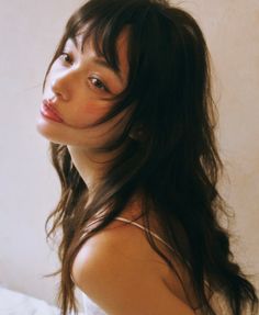 Woman with long dark hair and thin strap top looking over her shoulder