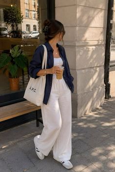 Woman in white wide leg pants and a navy blue shirt holding a drink on a street
