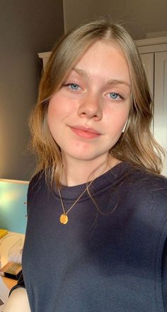 Young woman with blonde hair and blue eyes wearing a gold necklace indoors