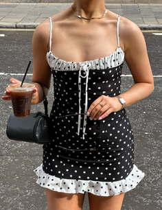 Woman in a black and white polka dot mini dress holding iced coffee and sunglasses