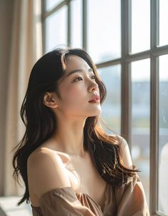 Woman with long dark hair in an off-shoulder top by a window