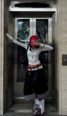 Person in a red cap and baggy shorts posing in front of an elevator