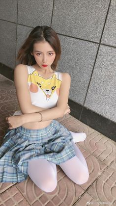 Woman in a crop top and plaid skirt with white tights sitting outdoors