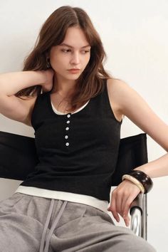 Woman with long hair wearing a tank top and sweatpants, sitting indoors