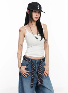 Woman in a black cap, white camisole, and loose jeans with a cross necklace