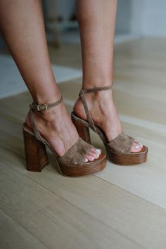 Person wearing brown suede platform heels with white pedicure on a wooden floor