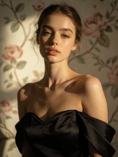 Woman in a black off-shoulder dress with soft lighting against floral wallpaper