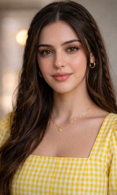 Woman with long brown hair wearing a yellow gingham dress and gold jewelry