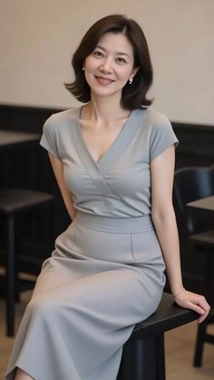Woman with short hair wearing a gray dress and earrings, smiling indoors