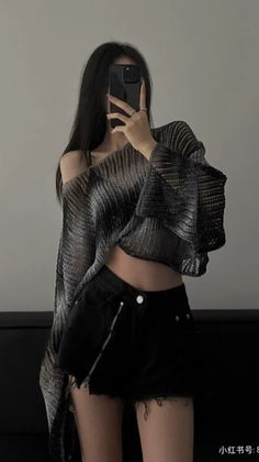 Woman with long black hair taking a mirror selfie in a crop top and shorts