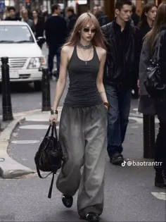 Woman with long hair and sunglasses walking on a street in baggy pants and a tank top