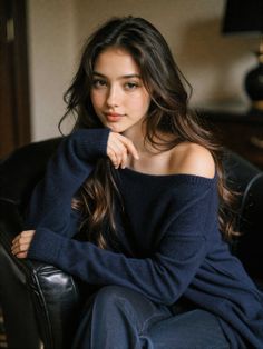 Woman with long dark hair wearing an off-shoulder sweater, sitting indoors