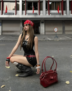 Woman in a red bandana and black outfit crouching on an outdoor street